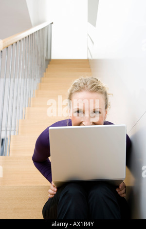 A mid adult woman sitting on a staircase using a laptop Stock Photo