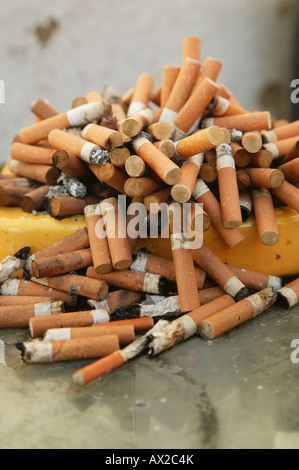 An overflowing yellow ashtray on a table Stock Photo
