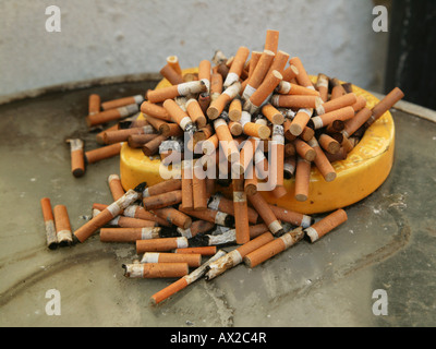 An overflowing yellow ashtray on a table Stock Photo