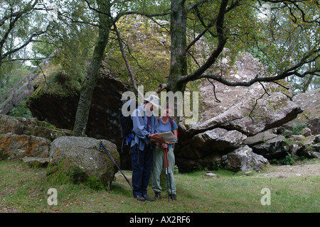 A male and female couple of walkers stop and read a map, wearing outdoor clothing. Bowder Stone, Lake District, Cumbria Stock Photo