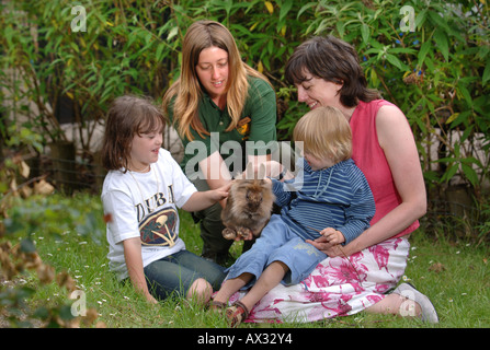 TWO CHILDREN WITH THEIR MOTHER MEET A RABBIT IN PETS CORNER AT LONGLEAT SAFARI PARK NEAR WARMINSTER WILTSHIRE Stock Photo