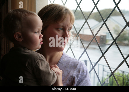 sad mother and baby boy looking out of window on wet day Stock Photo