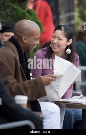 African American man and Asian American woman reading paper at outdoor cafe Stock Photo