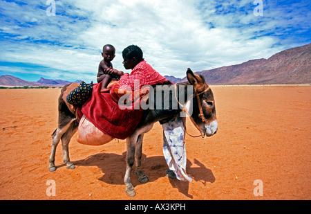 Himba Woman with baby Travelling on a Donkey Through Dry Marienfluss Kaokoland Kunene Region Namibia Stock Photo