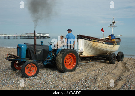 UK, Norfolk, Cromer, two fishermen on tractor hauling boat on beach Stock Photo