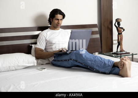 Young man working on a laptop in a bedroom Stock Photo