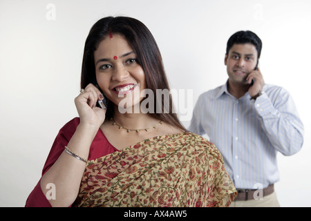 Portrait of a woman talking on a mobile phone and smiling with a man in the background Stock Photo