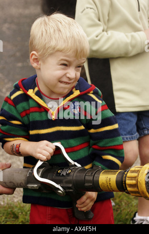 A young boy holding a fire hose putting out a fire with water spraying from the hose at a safety fair Stock Photo