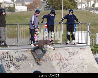 School children on a halfpipe in a skate park with safety helmets and elbow and knee pads on Stock Photo