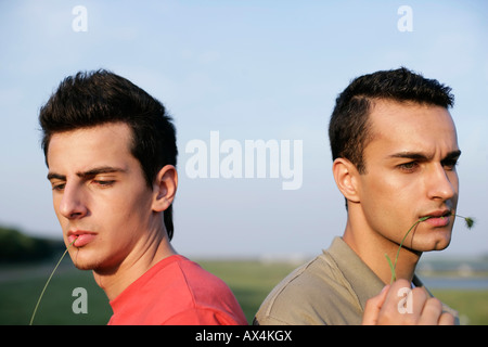 Two young men are sitting back to back, chewing blade of grass Stock Photo