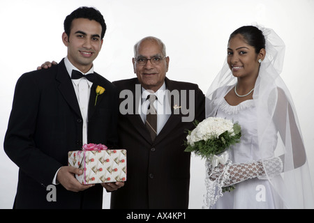 Portrait of a groom and a bride standing with their father and smiling Stock Photo