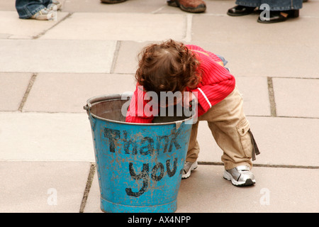 young boy putting money in a busker's bucket, with the words Thank You on the side Stock Photo