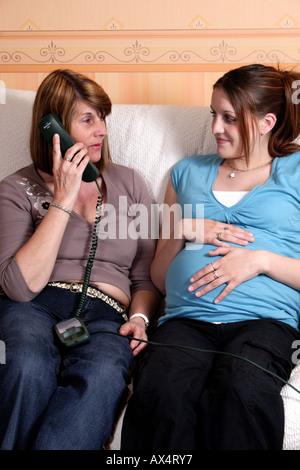 Young heavily pregnant woman with older woman/relative/midwife speaking on telephone Stock Photo