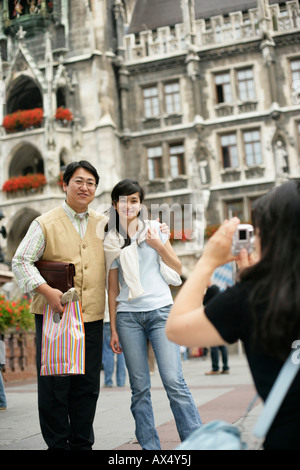 Young Asian woman taking a picture of an Asian man and a woman in front of the town hall of Munich, selective focus Stock Photo