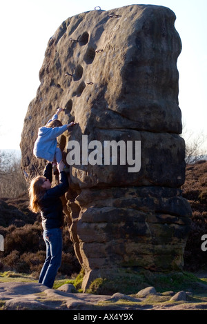 A mother helps a child climb the Cork Stone on Stanton Moor in the Peak District National Park, Derbyshire, England, UK Stock Photo