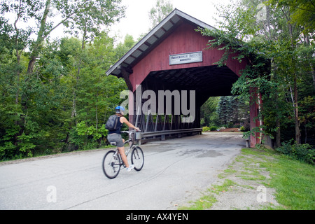 A young woman rides her bike through a covered bridge in the town of stowe, vermont Stock Photo