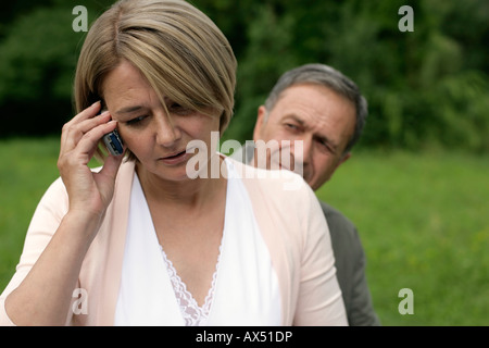 Mature woman using a mobile phone, man looking to her Stock Photo