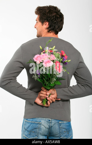 Young man holding bouquet of flowers behind back, smiling, rear view Stock Photo