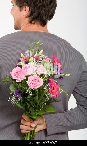 Young man holding bouquet of flowers behind back, smiling, close-up Stock Photo