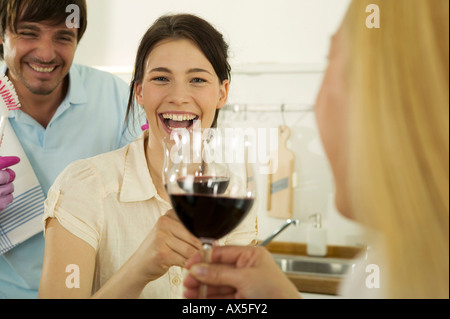 Three young people drinking wine in kitchen, smiling, close-up Stock Photo