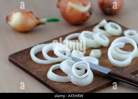 Sliced onions on a wooden cutting board, whole onions in the background Stock Photo