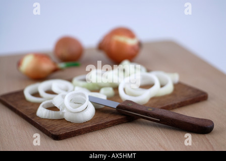 Sliced onions on a wooden cutting board, whole onions in the background Stock Photo