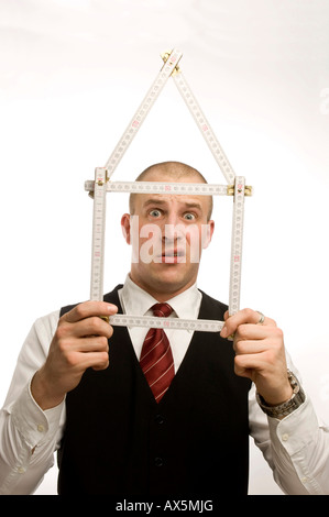 Man dressed in suit holding yardstick shaped into a house Stock Photo