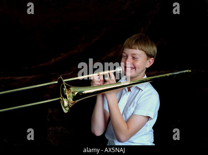 An 11 year old boy playing, or trying to play, the trombone. The musical instrument is almost bigger than he is. Stock Photo