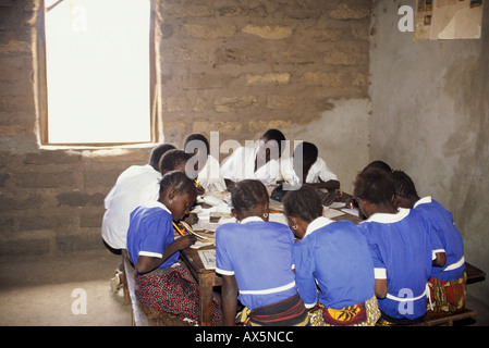 The Gambia. Schoolchildren sitting round a table in a mud brick school room working at their exercise books. Stock Photo