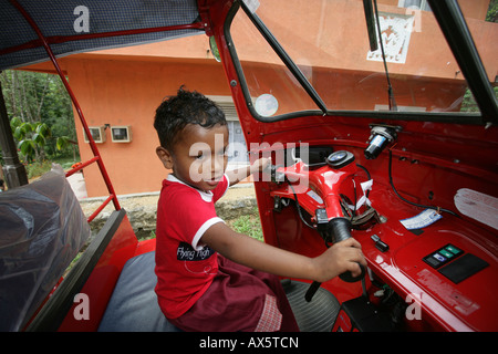 Small boy sitting at the wheel of a tuk-tuk in Hanwella, Sri Lanka, South Asia Stock Photo