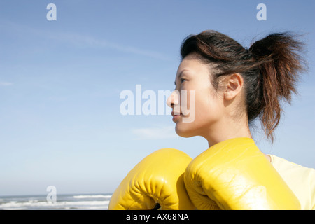 A side view of a woman wearing boxing gloves seen near the sea Stock Photo