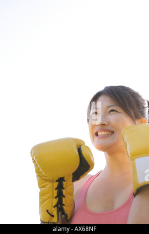An ecstatic woman wearing her boxing gloves seen under the sky Stock Photo