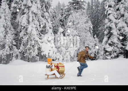 Man pulling woman holding present on sledge, side view Stock Photo