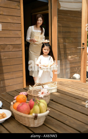 A small girl helping her mother to place meal on the wooden table Stock Photo