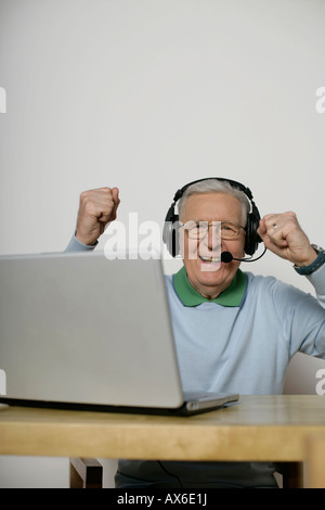 Senior man with headset cheering in front of a laptop, fully released Stock Photo