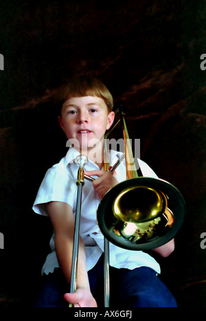 An 11 year old boy playing, or trying to play, the trombone. The musical instrument is almost bigger than he is. Stock Photo