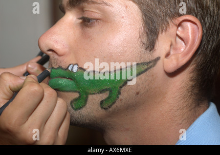 caricature of a green crocodile being painted on the face of a young white male Stock Photo