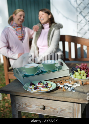 Breakfast on table with two women sitting on bench in background Stock Photo