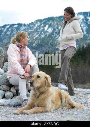 Two young women with dog at riverbank Stock Photo - Alamy