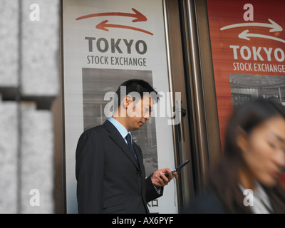 A Japanese businessman with mobile phone outside the Tokyo stock exchange dials a number while other business people pass in fro Stock Photo