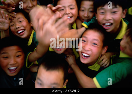 A crowd of Chinese children wave to the camera in a fit of excitement. Stock Photo