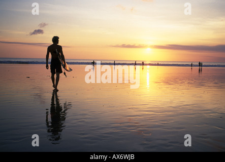 Sunset on Kuta Beach surfers carry their surfboards from the ocean after a long day riding the waves Stock Photo