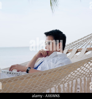 Side profile of a mid adult man lying in a hammock using a laptop Stock Photo