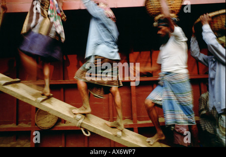 Workers unload a ship filled with sand by carrying the sand in wicker baskets on their heads Stock Photo