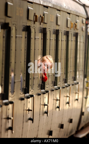 On the Bluebell Railway in East Sussex, a child looks out of the window as the steam train pulls out of Sheffield Park Station. Stock Photo