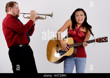 Stock Photograph of a man playing a trumpet into the ear of a teen girl with a guitar Stock Photo