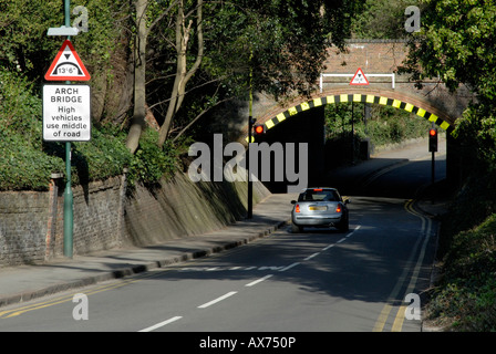 Low arch bridge with warning sign and high visibility markings and waiting car at red light, Cheam, south London, Surrey Stock Photo