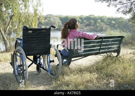 Rear view of a handicapped teenager girl sitting on a bench at lakeside Stock Photo