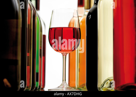 Glass of red wine between wine bottles, close-up Stock Photo