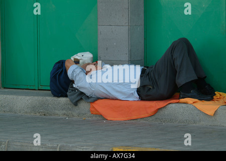 Siesta, spanish man takes a nap in the shade on the pavement during the heat of the midday sun Stock Photo
